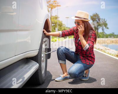 Traurige Frau könnte nicht das Rad entfernen. Ruft das Telefon auf die Garage und bittet um Hilfe bei der Reparatur. Stockfoto