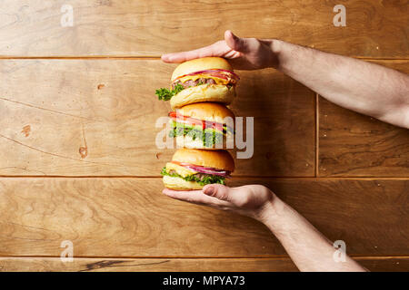 7/8 Hand des Menschen holding Cheeseburger über Holz- Tabelle Stockfoto