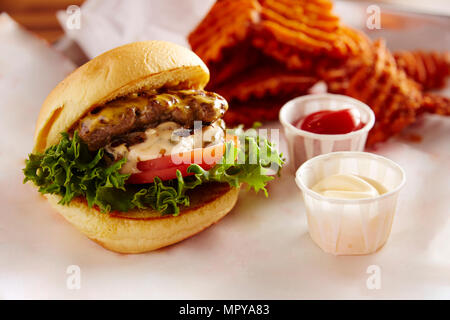 In der Nähe von Cheeseburger mit Pommes frites Waffeln in der Platte am Tisch serviert Stockfoto