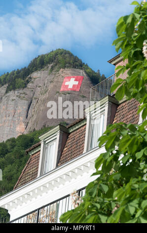 Schweizer Fahne auf der Seite eines Berges in der Nähe von Vitznau und Rigi Berg. Schweizer Fahne am Berghang mit zwei Fenster im Vordergrund. Stockfoto