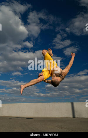 Austrickst, auf die Straße. Kampfsportarten Mann Salto vor barfuß. Bhudda Verkürzungen von unten gegen den Himmel. Stockfoto