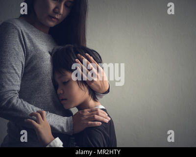 Traurig kleiner Junge von seiner Mutter zu Hause umarmte. Die Elternschaft, Liebe und Zusammengehörigkeit Konzept. Stockfoto