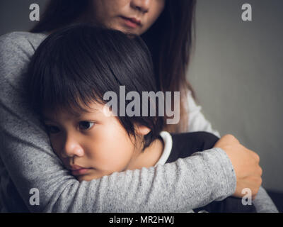 Closeup traurig kleiner Junge von seiner Mutter zu Hause umarmte. Die Elternschaft, Liebe und Zusammengehörigkeit Konzept. Stockfoto