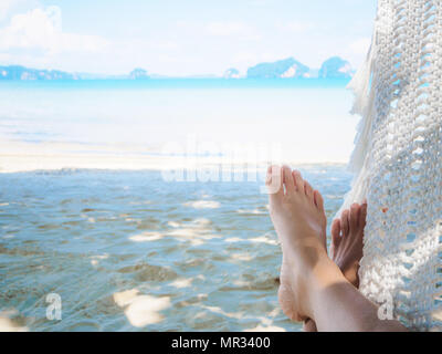 Closeup Frau, die Füße liegen auf Hängematte mit Bäumen und wunderschönen Meer/Strand. Stockfoto