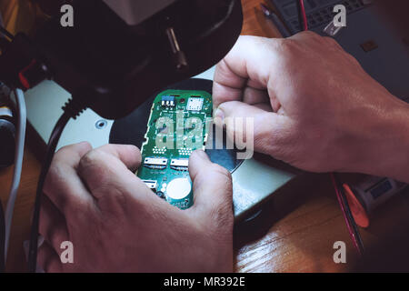 Close-up Fotos, Prozess der Handy reparieren. Telefon reparieren unter dem Mikroskop. Mobile Gebühr. Reparatur Gadgets zu Hause Nahaufnahme. Männliche Hände chec Stockfoto