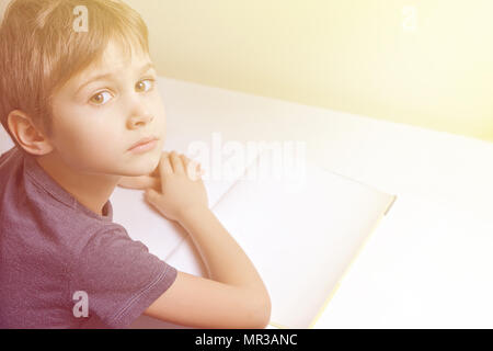 Junge sitzt am Tisch, lesen Buch und seine Hausaufgaben machen Stockfoto