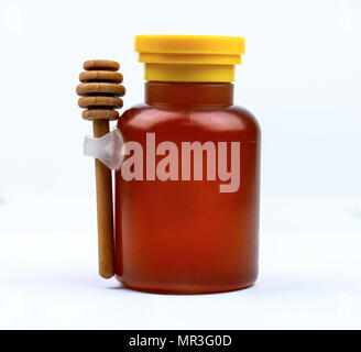 Honig im Glas Flasche mit gelbem Deckel und Holzstab auf weißem Hintergrund mit leeres Etikett isoliert. Köstliches Frühstück essen Konzept. Package Design Stockfoto