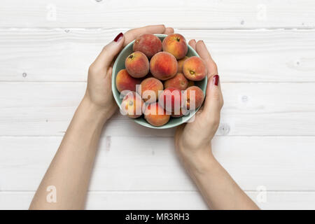 Tischplatte Szene mit weiblichen Händen hält eine Schüssel mit Pfirsichen Stockfoto