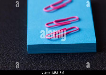 Stapel von blauen Aufkleber und rosa Büroklammern auf schwarzem Hintergrund Stockfoto