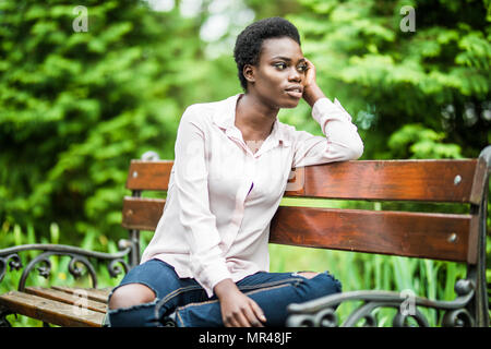 Portrait von afrikanische amerikanische Frau mit Afro Frisur sitzen auf der Holzbank outdoor. Stockfoto
