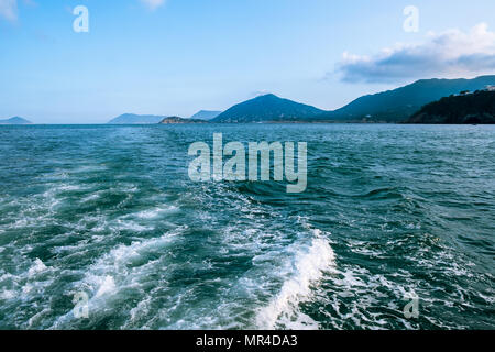 Welle mit weißer Schaum auf der Oberfläche hinter sich schnell bewegende Motorboot oder Yacht. Kleine Inseln im Dunst am Horizont. Blue Sky vor Sonnenuntergang. Stockfoto