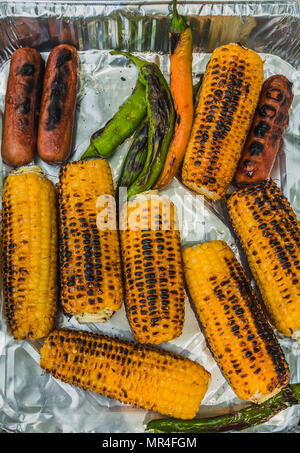 Blick von oben auf die gegrillten Maiskolben, grüner Chili und Würstchen auf Einweg Aluminium Lebensmittelverpackungen. Stockfoto