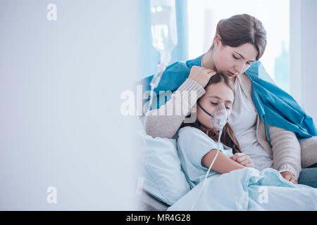 Sorge Mutter kümmert sich um ihre Tochter, die eine Sauerstoffmaske tragen im Krankenhaus Stockfoto