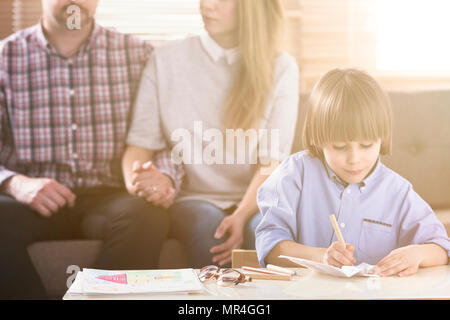 Mann und Frau, Hände auf ein Sofa und einen Jungen vor Zeichnen von Bildern durch einen Tisch während einer Familie Psychotherapie Sitzung. Vorderansicht. Flare. Blurre Stockfoto