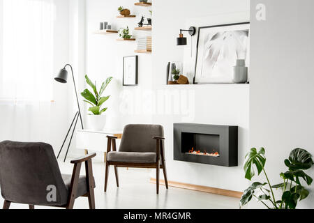 Grauen Sesseln neben dem Kamin in White Apartment Interieur mit Anlage, Poster und eine Lampe. Real Photo Stockfoto