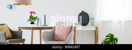 Puder Pink Kissens auf einem grauen Sessel neben einem Tisch mit Einrichtung in Weiß Wohnzimmer innen stehend Stockfoto