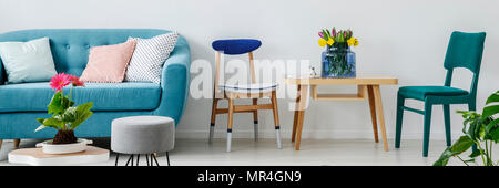 Weiß Wohnzimmer Interieur mit frischen Blumen auf Holztisch und blaue Couch mit dekorativen Kissen Stockfoto