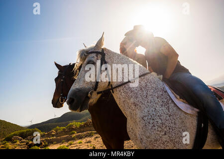 Liebe Szene zwischen junge Schöne coule reiten zwei nette Pferde in der Natur. Windmühle für grüne Energie und bessere Zukunft im Hintergrund. Alternativ Stockfoto