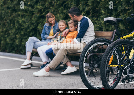 Casual Familie sitzt auf der Bank im Park, selektiver Fokus auf Fahrrädern in Vordergrund Stockfoto