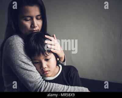 Traurig kleiner Junge von seiner Mutter zu Hause umarmte. Die Elternschaft, Liebe und Zusammengehörigkeit Konzept. Stockfoto