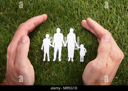 Erhöhte Ansicht einer menschlichen Hand Schutz der Familie Papier schneiden Sie auf grünem Gras Stockfoto