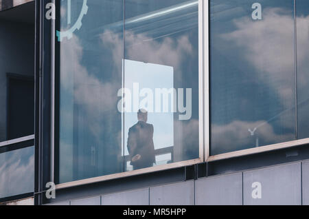 Business Mann über das Fenster in einem modernen Gebäude mit Reflexion der Himmel und Wolken im Windows Stockfoto