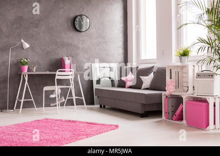 Geräumiges Zimmer in Grau, Rosa und Weiß mit Schreibtisch, Büro, Lampe, Sofa und Bücherregal Stockfoto