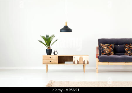 Schwarze Lampe oben Holzschrank mit Palm und Uhr Neben dunklen Sofa im Wohnzimmer Interieur mit Teppich Stockfoto