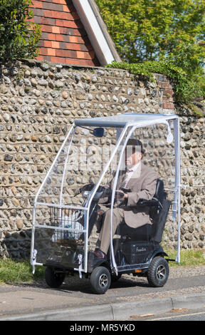 Älterer Mann reiten Schlitzohr Frontier elektrische Mobilität scooter mit einem Schutzdach auf dem Bürgersteig in Großbritannien. Stockfoto