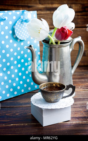Kaffee in Silver Cup gegen Geschenktasche und Tulpen auf Schwarz Stockfoto