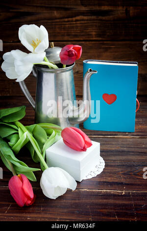 Blumenstrauß aus Tulpen, Notepad mit Herz, Pott Kaffee und weißen Geschenkbox auf Schwarz Stockfoto