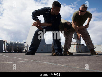 Master at Arms 1. Klasse William Casselle der USS-Mesa Verde LPD (19), und Gunnery Sgt. Arvin Manning, Personal noncommissioned Officer zuständig für die Strafverfolgung Loslösung, 24 Marine Expeditionary Unit (MEU), vergleichen und Ähnlichkeiten in Protokoll zwischen den beiden Diensten während der Ausführung eines 2-Mann arm Manipulation Technik auf Sgt. Steven Eakes, ein militärischer Polizist, während eine nicht tödliche Klasse als Teil des Master-at-arms Ausbildung an Bord des amphibious Transport dock Schiff 17. Mai 2017. Die 24. MEU ist mit dem Bataan Amphibious Ready Gruppe unterwegs in der Unterstützung der Sicherheit des Seeverkehrs operatio Stockfoto