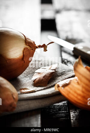 Immer noch leben der Zwiebel auf einem Sack mit Zwiebel Häuten um und ein Messer im Hintergrund auf Holzbrettern beleuchtete gegen das Licht. Dunkle Moody st Stockfoto