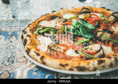 Im Sommer Mittag- oder Abendessen. Frisch gebackene italienische vegetarische Pizza mit Gemüse und frischem Basilikum über orientalische Fliesen Hintergrund, Nahaufnahme Stockfoto