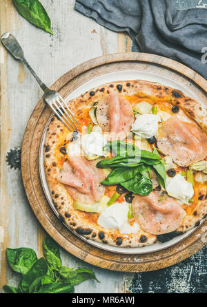 Italienische Mittag- oder Abendessen. Flachbild-lay der frisch gebackene Pizza mit Artischocken, geräucherte Türkei Schinken, Oliven, Frischkäse, grüne Blätter Basilikum auf Fach über Rus Stockfoto