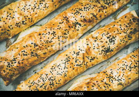 Flachbild-lay von frisch gebackenem Türkischem borek Gebäck Brötchen mit Spinat, Fetakäse und schwarzkümmel Samen über Backpapier, Ansicht von oben. Traditionelle Osten Med Stockfoto