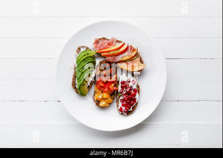 Vielzahl von Bruschetta mit avecado, Schinken, Tomaten und Granatapfel Samen auf weiße Platte Stockfoto