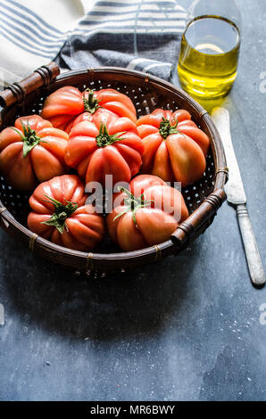 Frisch gepflückte Rindfleisch Tomaten in einem Weidenkorb vor einem dunklen Hintergrund. Stockfoto