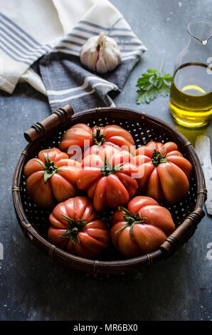 Frisch gepflückte Rindfleisch Tomaten in einem Weidenkorb vor einem dunklen Hintergrund. Stockfoto