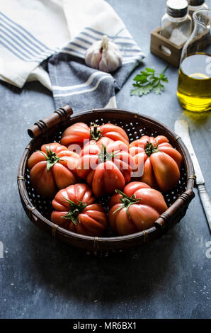 Frisch gepflückte Rindfleisch Tomaten in einem Weidenkorb vor einem dunklen Hintergrund. Stockfoto