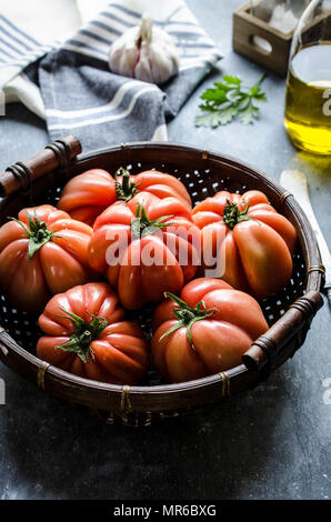 Frisch gepflückte Rindfleisch Tomaten in einem Weidenkorb vor einem dunklen Hintergrund. Stockfoto