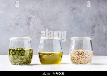 Gläser mit traditionellen Basilikum Pesto, Olivenöl, Pinienkerne am Küchentisch mit weißer Bettwäsche Tischdecke. Platz kopieren Stockfoto