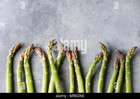 Roh ungekocht organischen grünen Spargel in der Zeile über grau Textur Hintergrund. Ansicht von oben, kopieren. Stockfoto