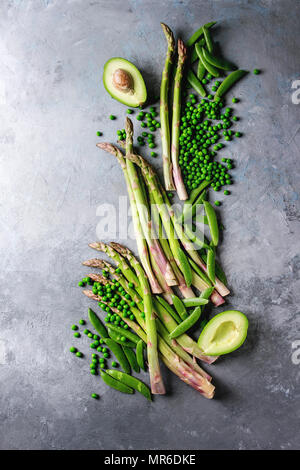 Vielzahl von Roh ungekocht organische Junge grüne Gemüse, Spargel, Erbsen, pod Erbse, Avocado über grau Textur Hintergrund. Ansicht von oben, kopieren. Gesunde e Stockfoto