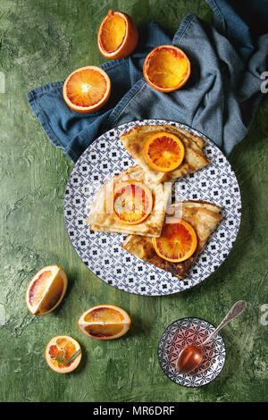 Hausgemachte crepes Pfannkuchen serviert in Weiß dekorieren Keramikplatte mit blutigen Orangen und Rosmarin Sirup mit in Scheiben geschnittenen sizilianischen Rotwein orangen und blauen Tuch Stockfoto