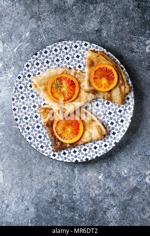 Hausgemachte crepes Pfannkuchen serviert in Weiß dekorieren Keramikplatte mit blutigen Orangen und Rosmarin Sirup mit in Scheiben geschnittenen sizilianischen Rotwein Orangen über blauen Text Stockfoto