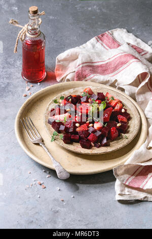 Rote Bete und Erdbeere, Salat mit Oregano Kräuter und Nüsse auf Keramikteller mit Tuch und eine Flasche Obst ocet über grau Textur Hintergrund serviert. Er Stockfoto