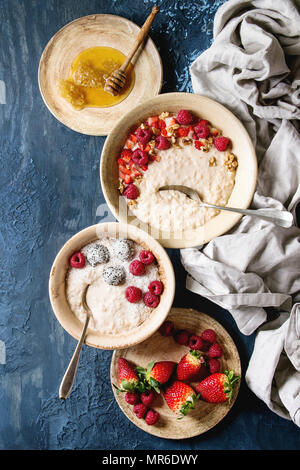 Süßen Reisbrei Pudding in Keramik Platte mit Beeren Erdbeere und Himbeere, Walnüssen, Honig auf Tuch über blaue Textur Hintergrund. Ansicht von oben, sp Stockfoto