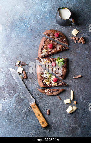 In Scheiben geschnittene hausgemachte süße Dessert Schokolade Pizza mit verschiedenen Schokoladen, Himbeeren und Minze mit Messer und Zutaten oben über blaue Textur hinterg Stockfoto