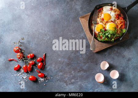 Traditionelle israelische Gerichte Shakshuka. Spiegelei mit Gemüse Tomaten und Paprika in gusseisernen Pfanne auf Holzbrett mit Koriander Kräuter ove Stockfoto